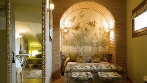 Un dormitorio con chimenea de ladrillo, una cama con ropa de cama floral y un espejo con marco decorativo.