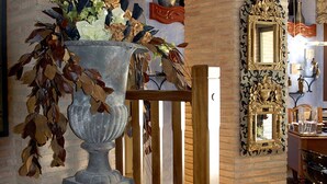 Un vestíbulo con una urna de piedra llena de plantas secas, un portón de madera y un espejo en la pared.