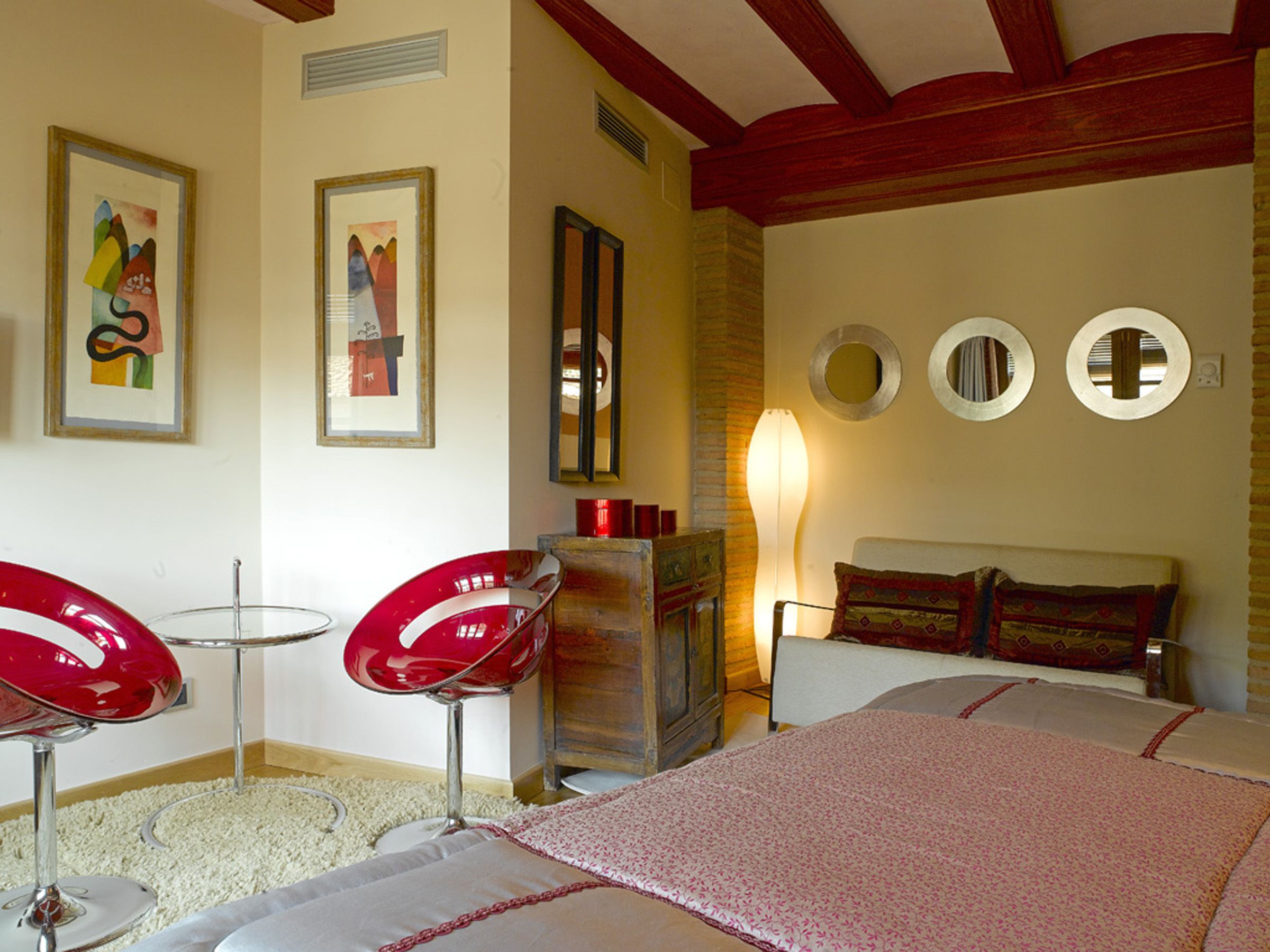 Een slaapkamer met een bed, twee rode stoelen, een kaptafel en drie spiegels aan de muur.