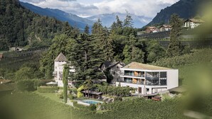 Una casa moderna de dos pisos con un balcón grande, rodeada de abundante vegetación y montañas al fondo.