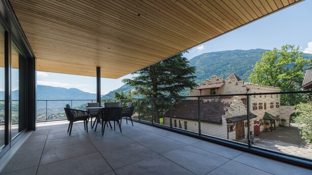 Un balcón con techo de madera, una mesa con sillas y vistas a un paisaje montañoso y edificios tradicionales.