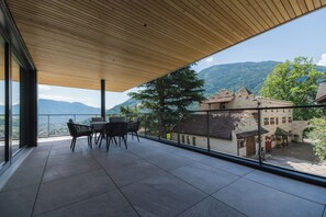 A balcony with a wooden ceiling, a table with chairs, and a view of a mountainous landscape and traditional buildings. - SCHLOSS PLARS Wine & Suites (Lagundo)