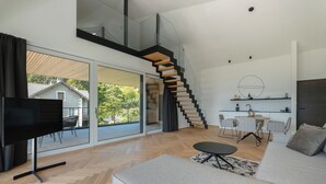 Una sala moderna con un televisor de pantalla plana grande, un sofá, un comedor con una mesa y sillas, y una escalera que lleva a un nivel superior.