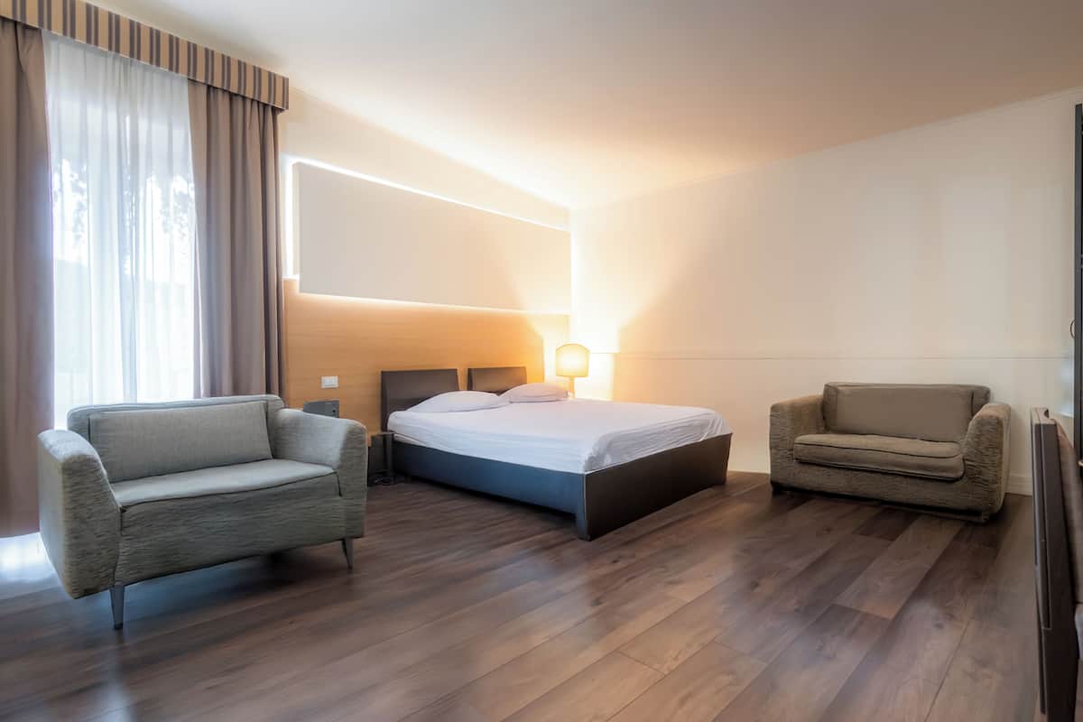 Een hotelkamer met een bed, twee fauteuils, een nachtkastje en een wandlamp.