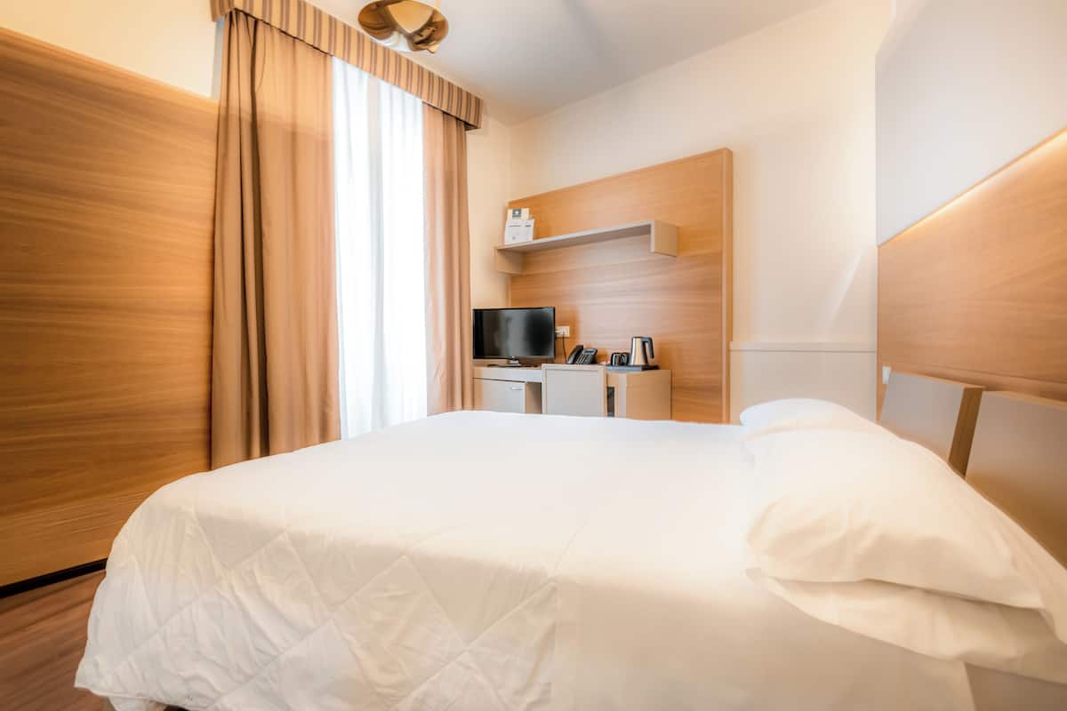 Een hotelkamer met een groot bed, een bureau met een televisie en een kleine keukenhoek.