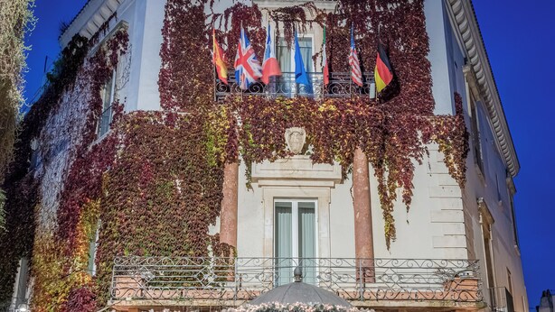A historic building with ivy-covered walls, a classic entrance, and flags of the UK, USA, and Germany. - Hotel San Nicola (Altamura)