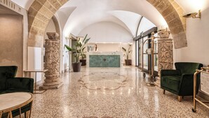 A lobby with a marble floor, green velvet chairs, a reception desk, and stone columns. - Hotel San Nicola (Altamura)