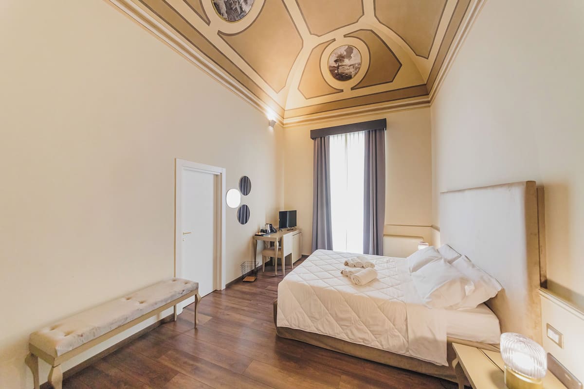 Een hotelkamer met een bed, een bureau, een bankje en een raam met gordijnen.