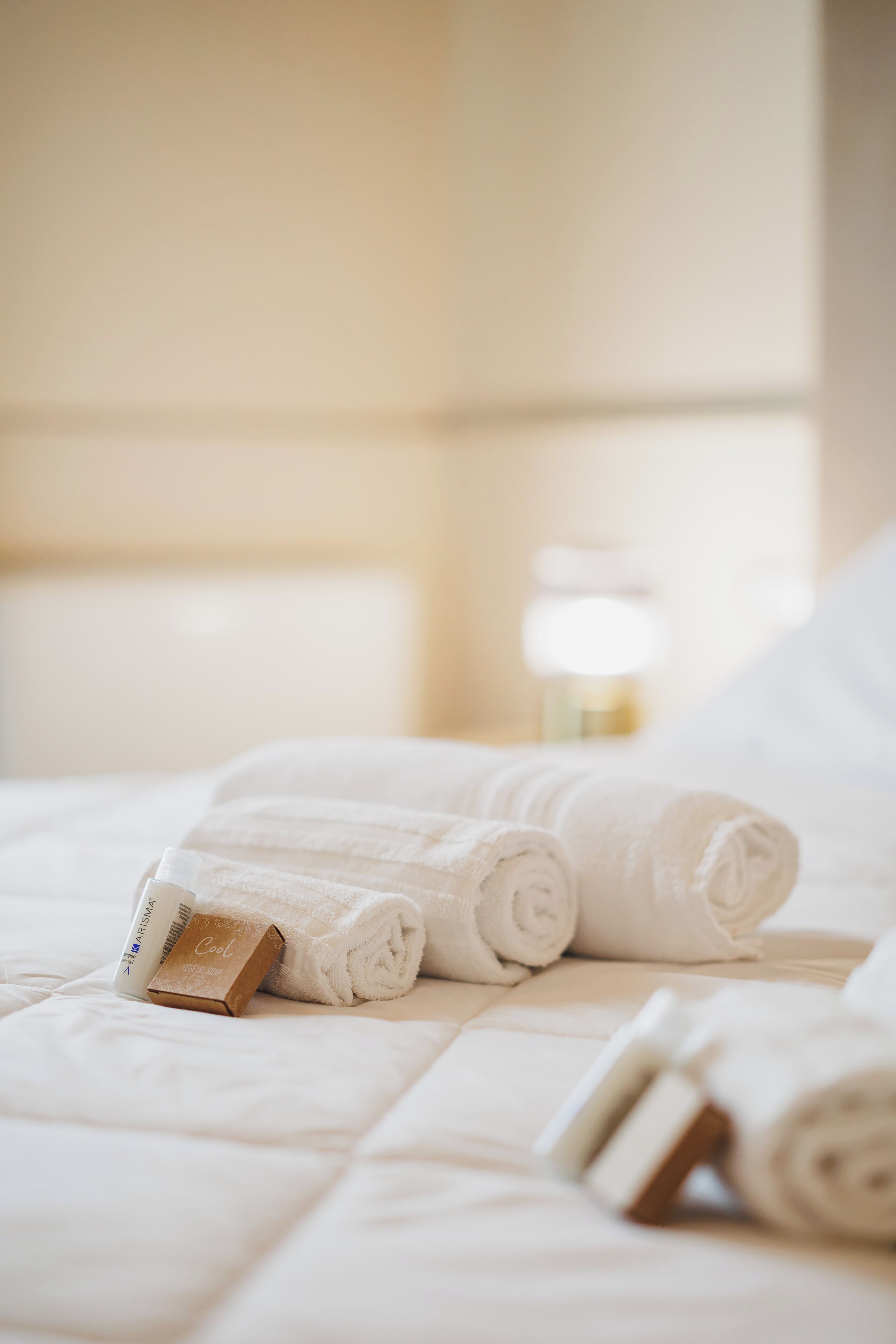 A neatly made bed with rolled white towels and a bottle of lotion.
