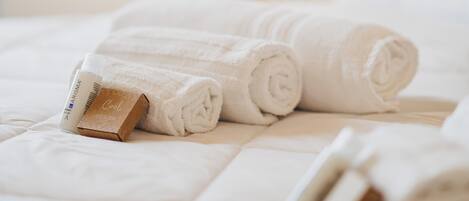 A neatly made bed with rolled white towels and a bottle of lotion.