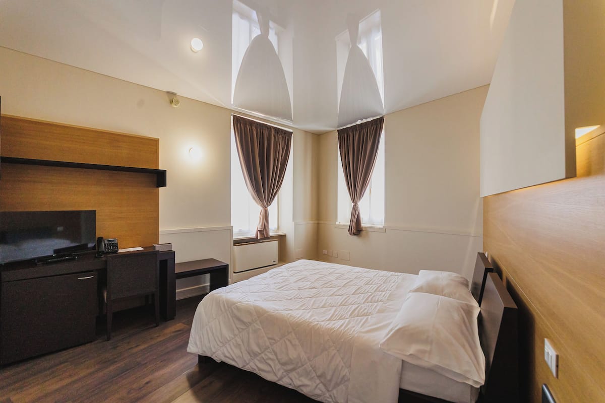 Een hotelkamer met een bed, bureau, televisie en een raam met gordijnen.