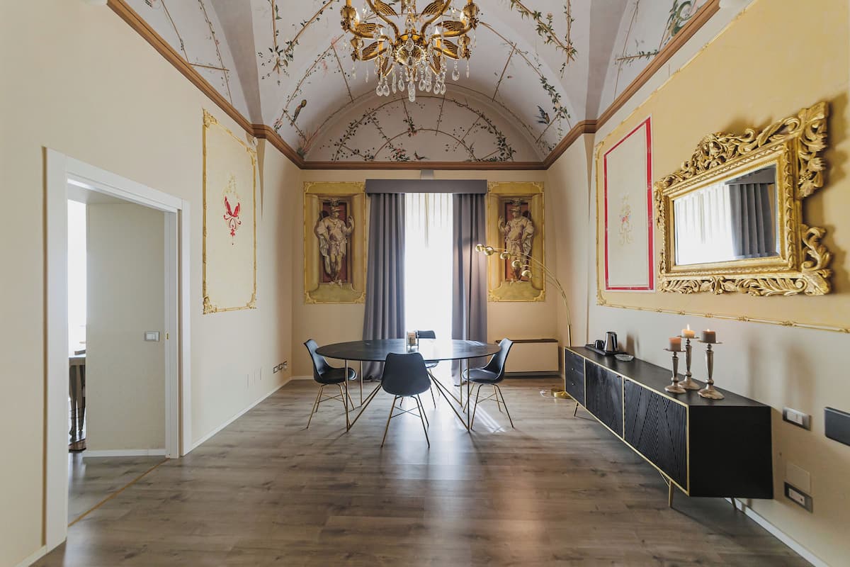 Een eetkamer met een ronde tafel, zwarte stoelen, een zwarte console en een grote, decoratieve spiegel.