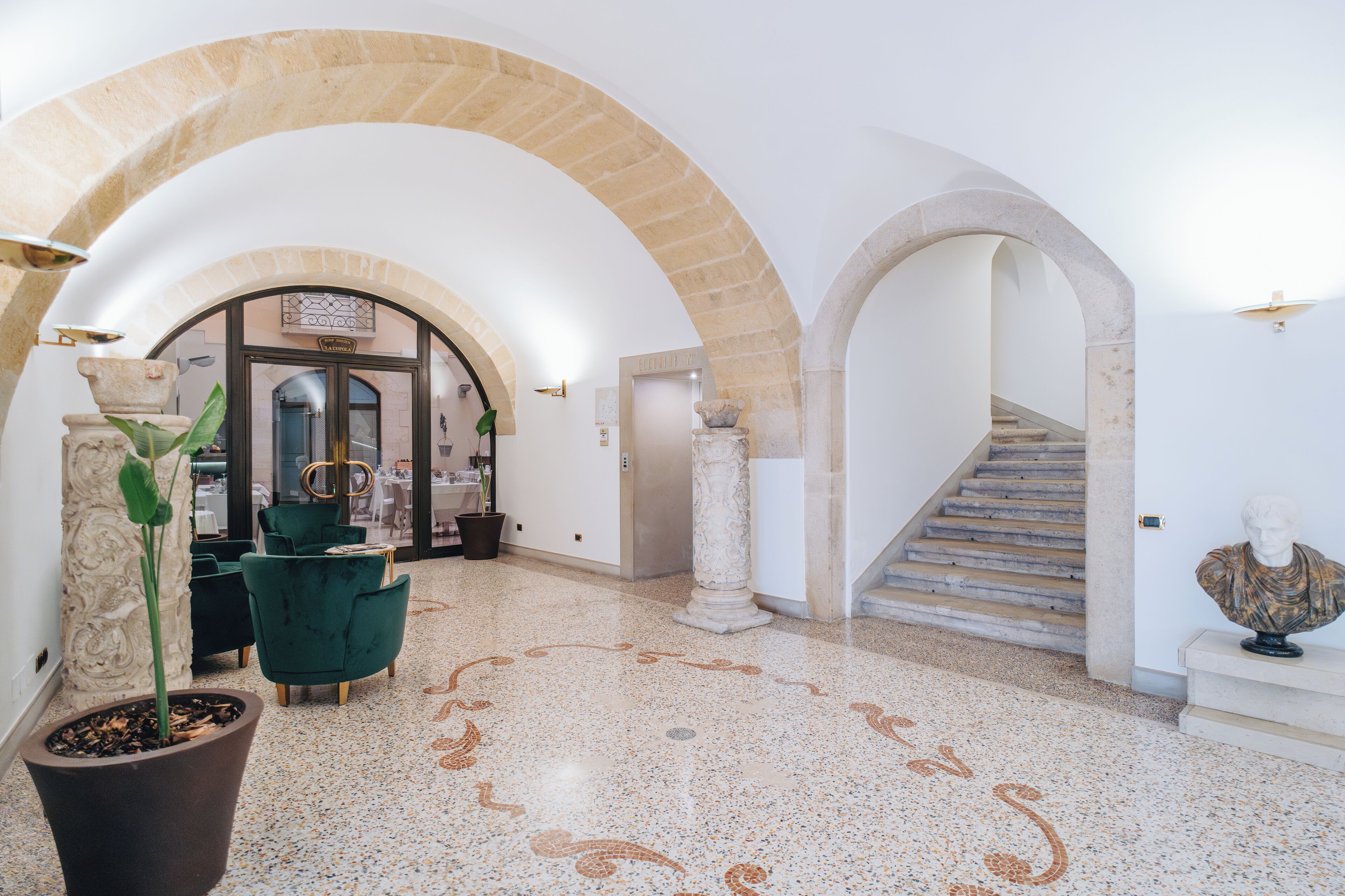 Un vestíbulo amplio con techos altos en arco, piso de terrazo y una escalera que conduce a un nivel superior.