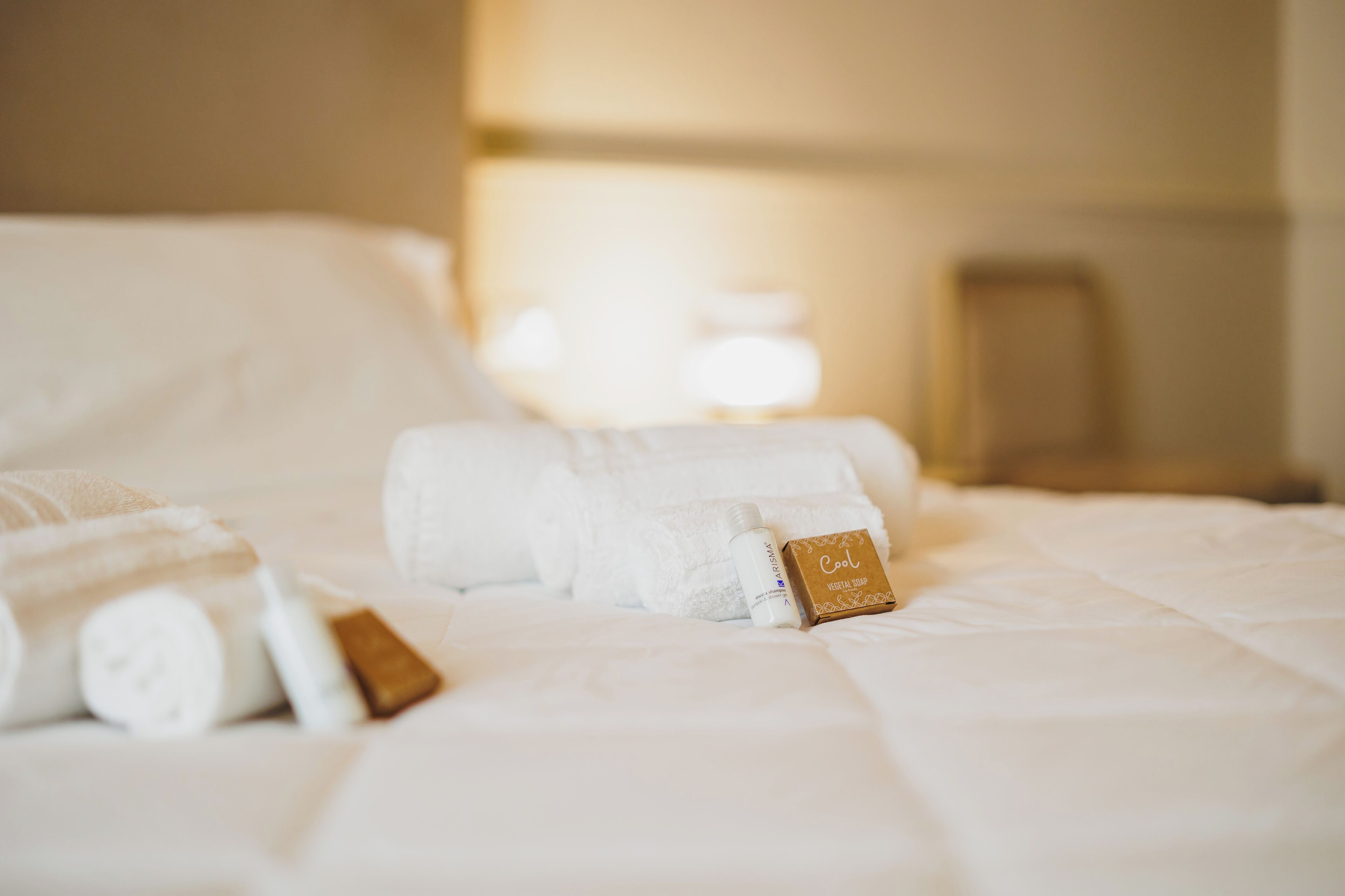 A neatly made bed with rolled white towels and a bottle of lotion.