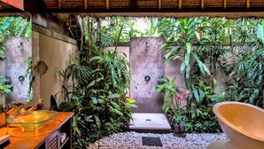 A bathroom with a glass bowl sink, a small bathtub, and a large terracotta pot. - Amori Villas (Ubud)