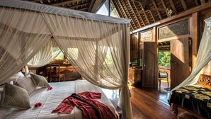 A bedroom with a canopy bed, wooden flooring, and a view of the outdoors. - Amori Villas (Ubud)