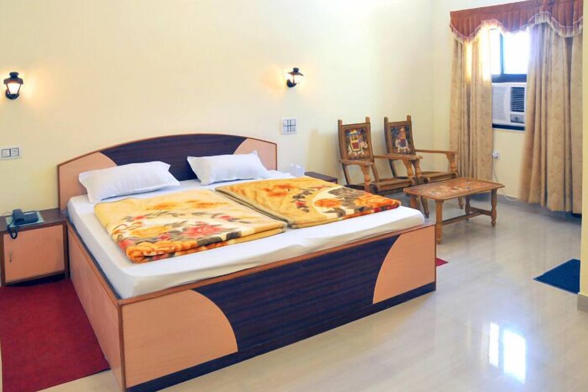 A neatly made bed with a floral bedspread, a wooden nightstand with a lamp, and a chair with a painting.