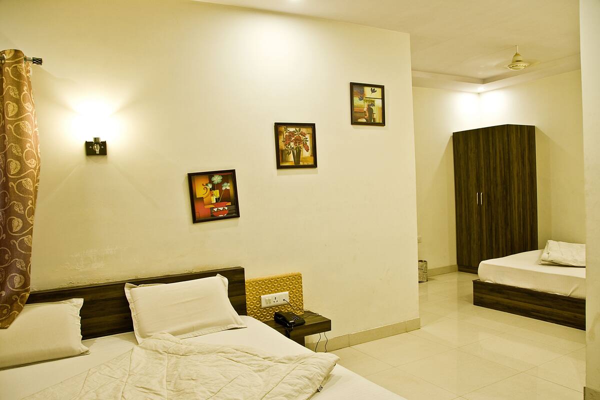 A hotel room with a bed, bedside table, and a nightstand with a phone. There are wall-mounted lights and framed pictures on the wall.