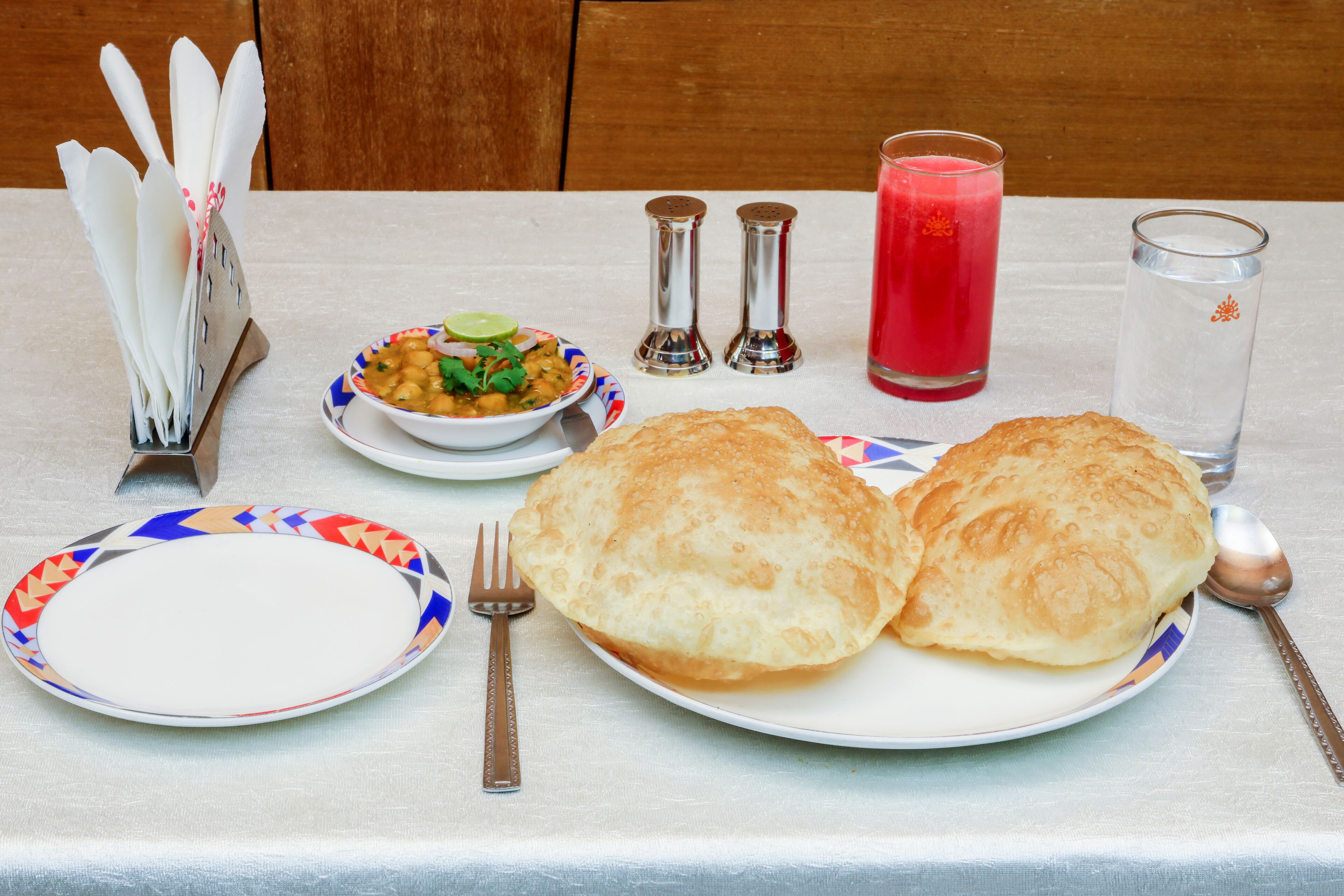 Une table dressée avec une assiette de nourriture, un verre de boisson rouge et un verre d’eau.