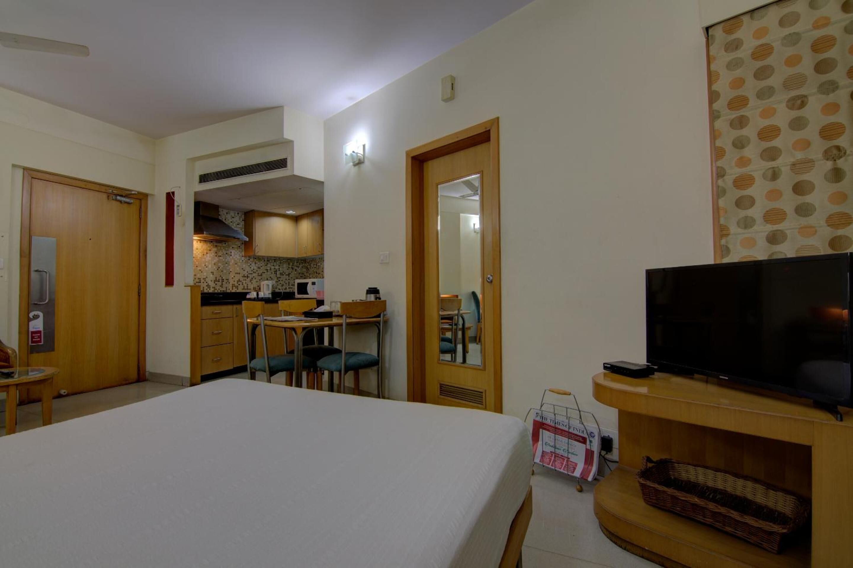 A hotel room with a bed, a TV, a small table, a chair, a kitchen area, and a bathroom.
