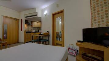 Habitación de hotel con cama, televisión, mesita pequeña, silla, zona de cocina y baño.