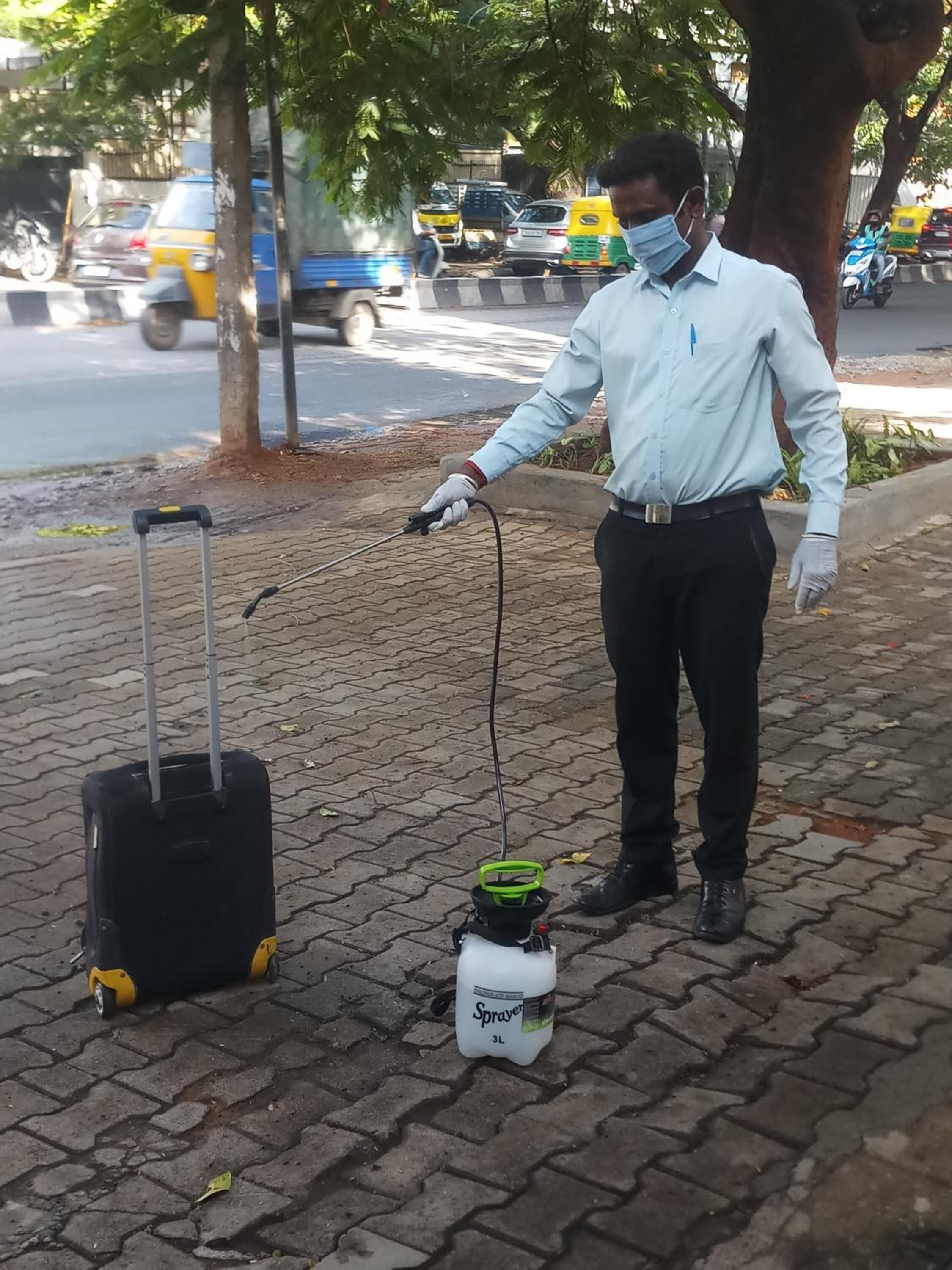 Una persona de pie sobre un área pavimentada, con una maleta y un pulverizador.