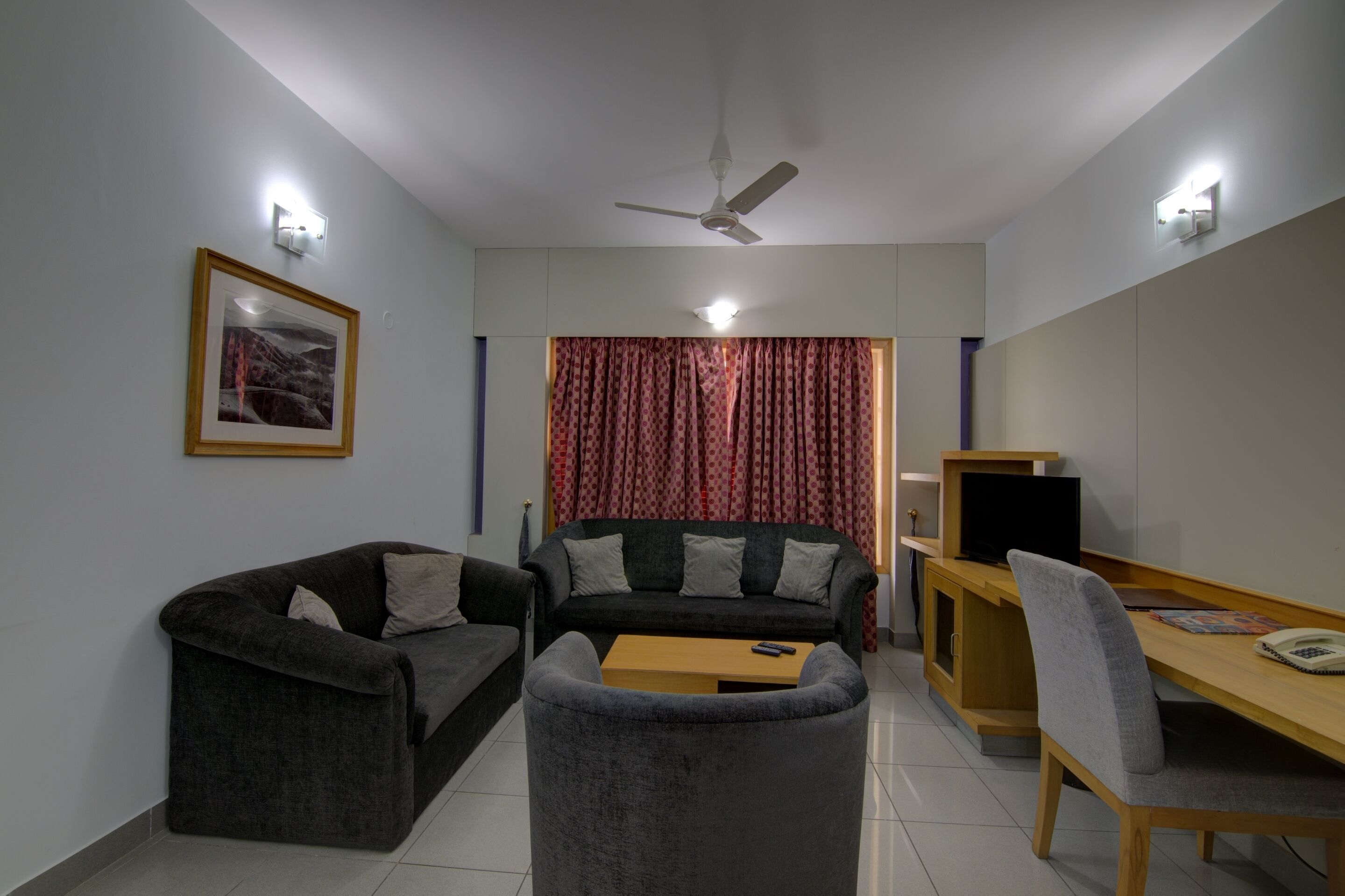 A compact living space with two sofas, a small table, a TV, and a desk with a chair.