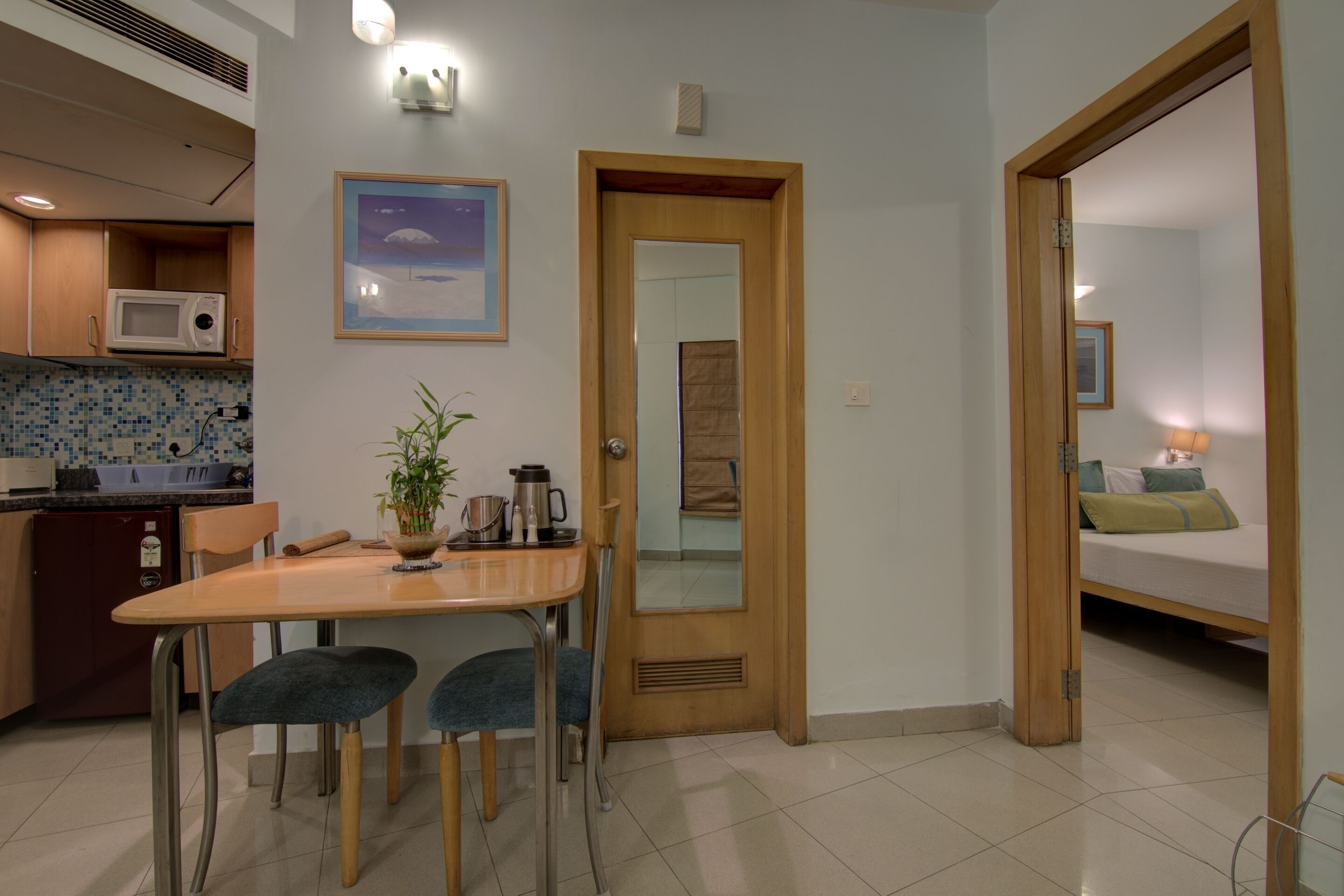 Un espace de vie compact comprenant un coin cuisine, un coin repas avec une table et des chaises, et une chambre avec un lit et une table de chevet.