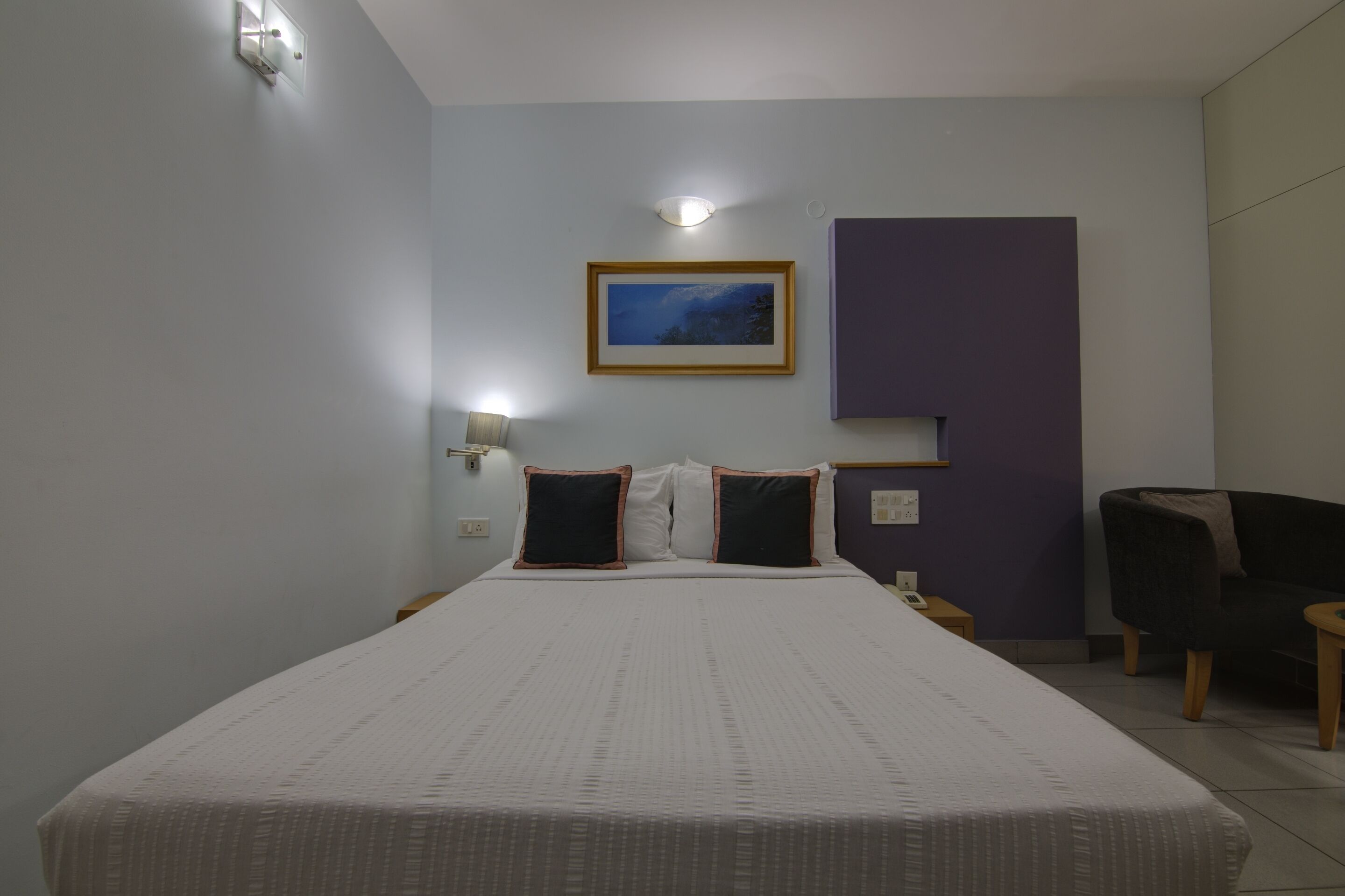 Habitación de hotel con una cama grande, una mesita de noche, una silla y una lámpara fijada a la pared.