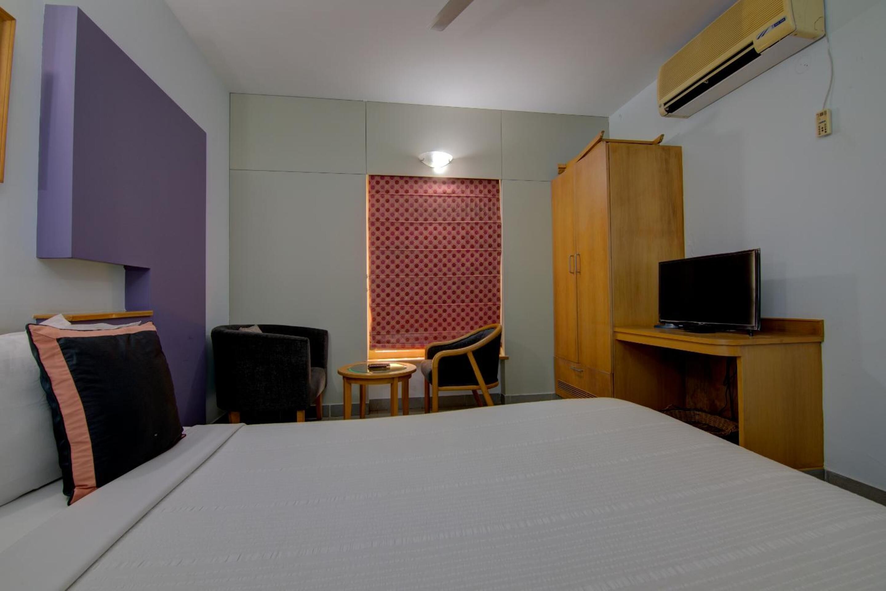 A hotel room with a bed, a desk with a television, a chair, and a wardrobe.