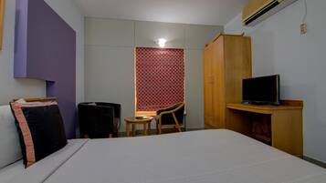 Una habitación de hotel con una cama, un escritorio con televisor, una silla y un armario.