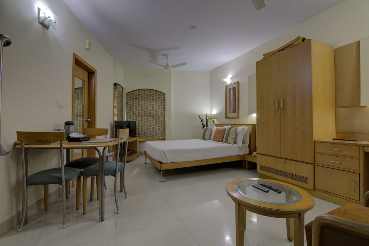 A bedroom with a bed, a desk, a chair, a wardrobe, and a small table with a remote control.