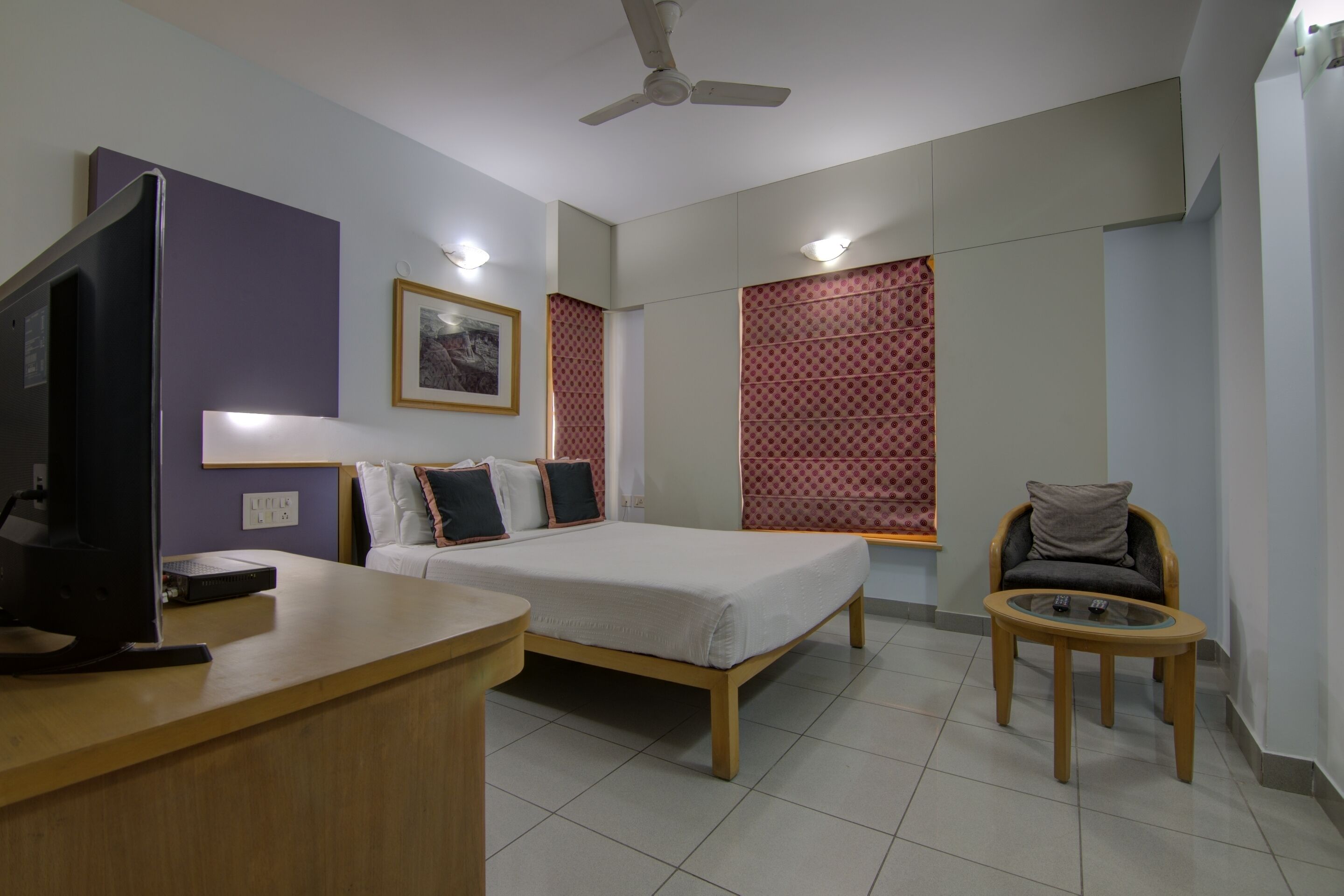 A hotel room with a bed, a desk, a chair, a television, and a ceiling fan.