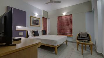 A hotel room with a bed, a desk, a chair, a television, and a ceiling fan.