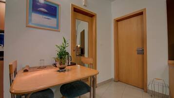 Un área de comedor con una mesa de madera, dos sillas, una planta en maceta y un cuadro en la pared.