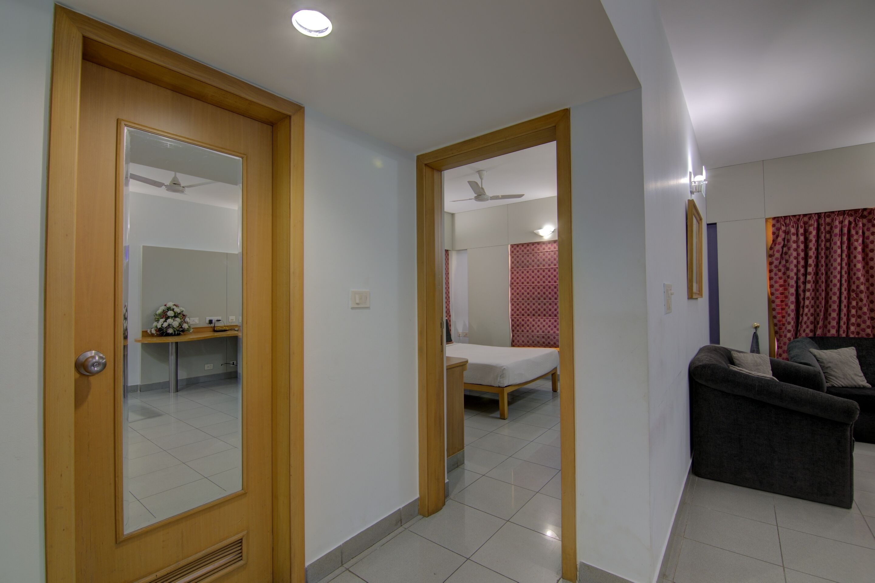 A modern room with a wooden door, a bed, a sofa, and a small table with a vase.