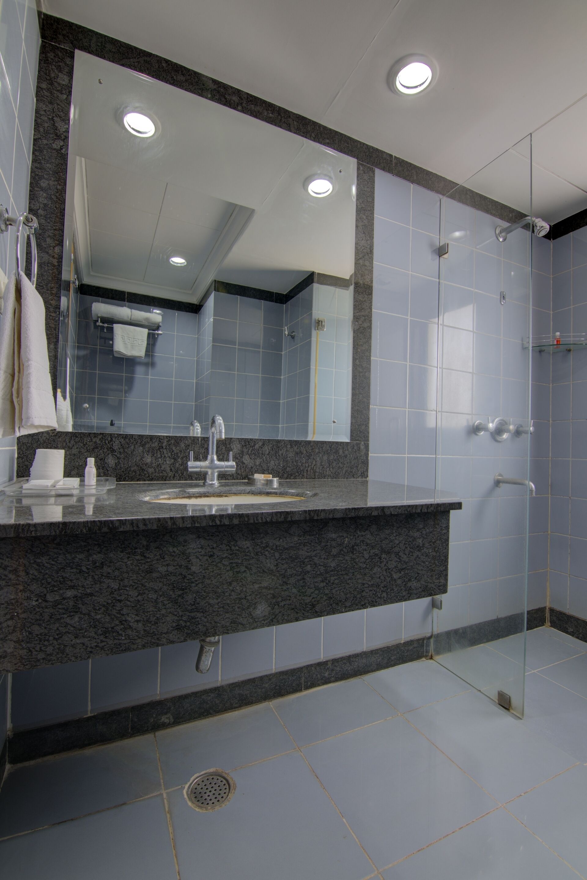 Un bagno moderno con un piano di lavoro in granito, un grande specchio e cabina doccia in vetro.