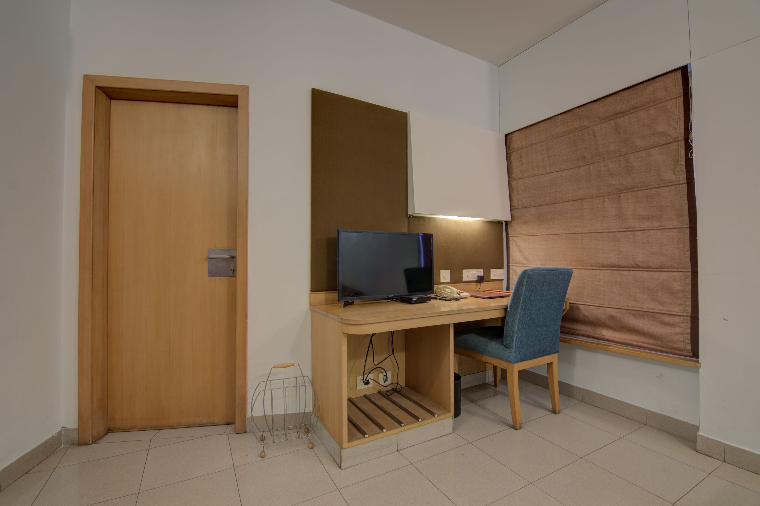 A compact room with a wooden desk, a chair, a computer, and a window with a blind.