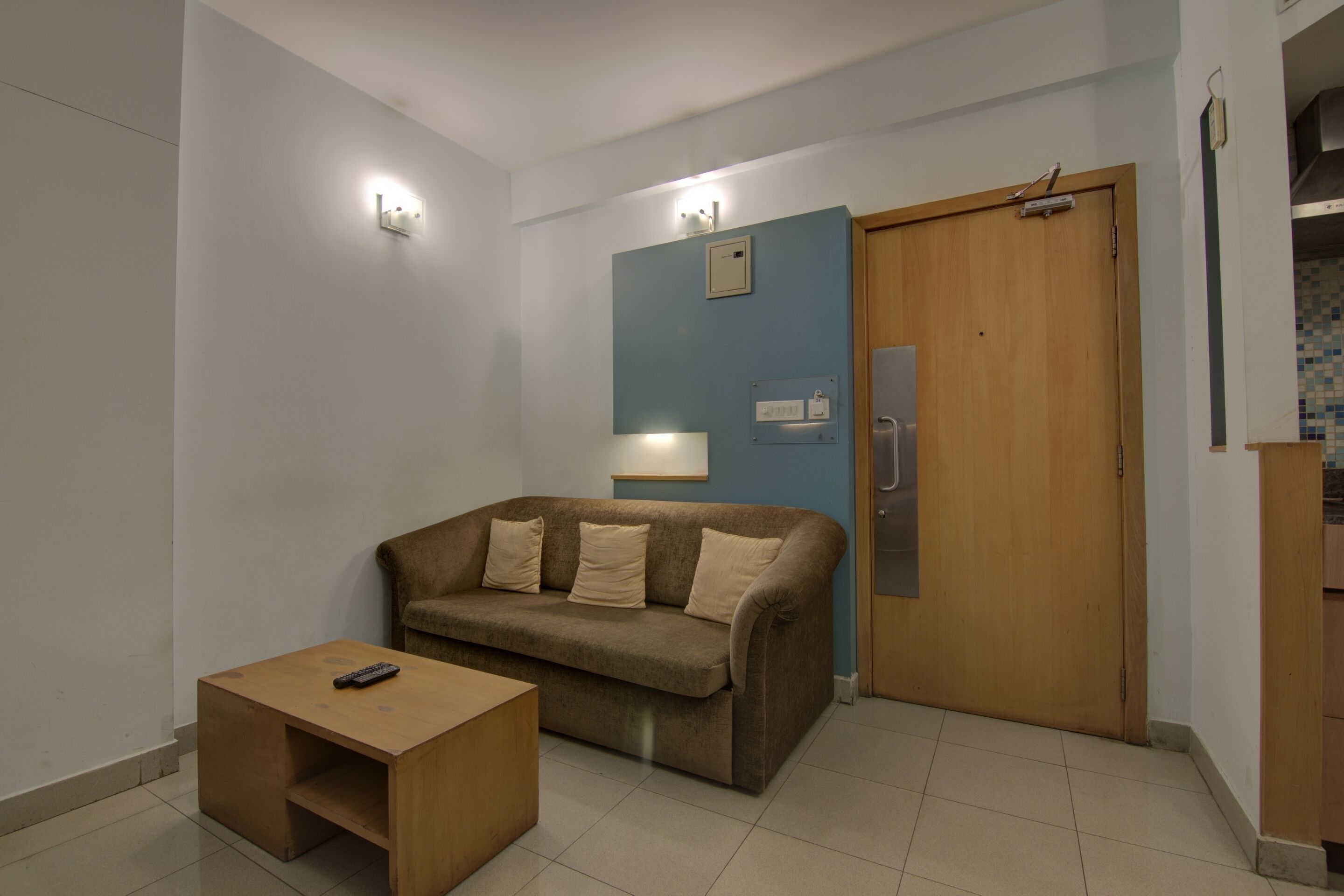 A small, well-lit room with a brown sofa, a wooden side table, and a wooden door.