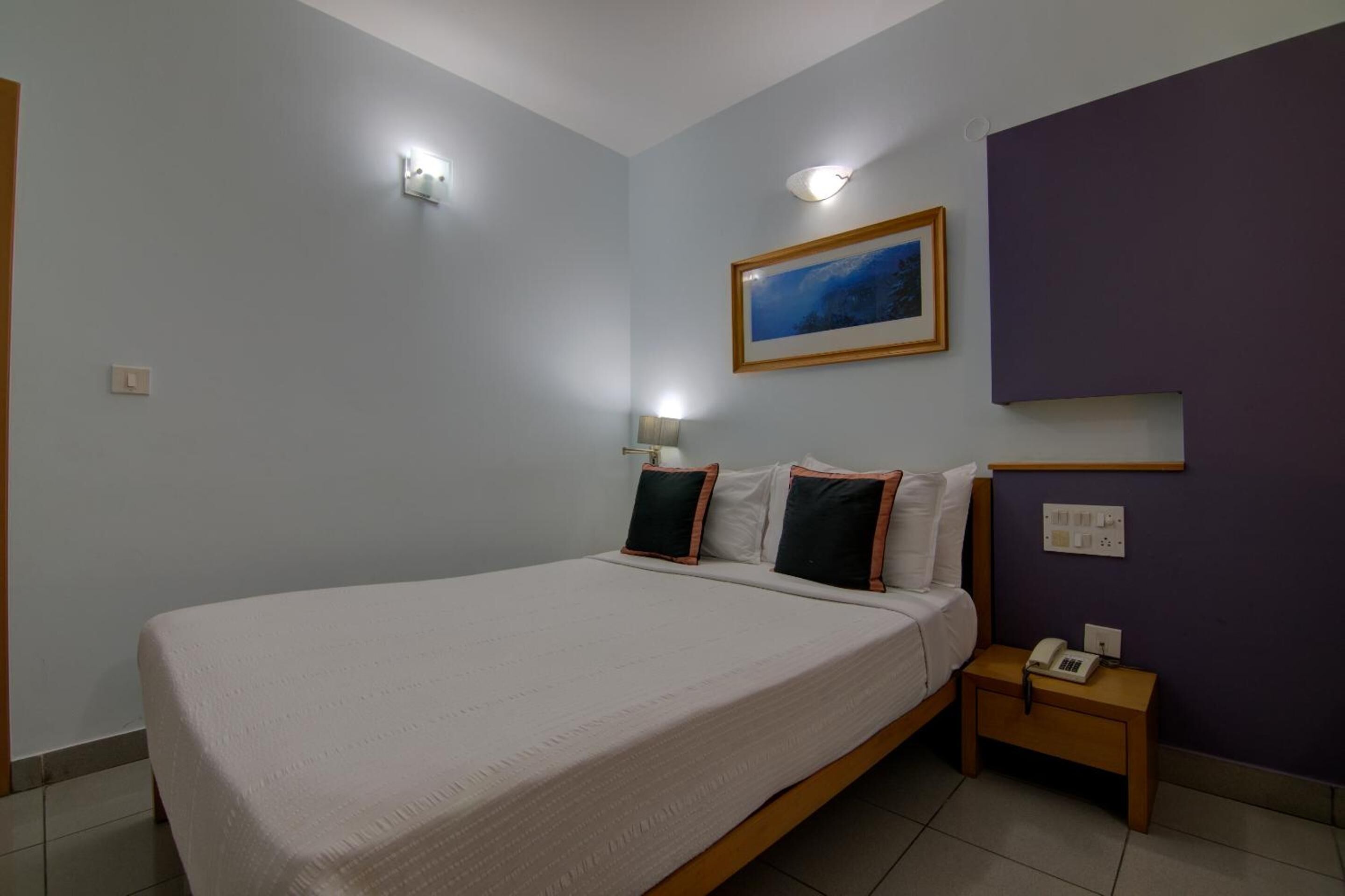 Ein Schlafzimmer mit Bett, Nachttischlampen, einem Nachttisch und einem Bild an der Wand.
