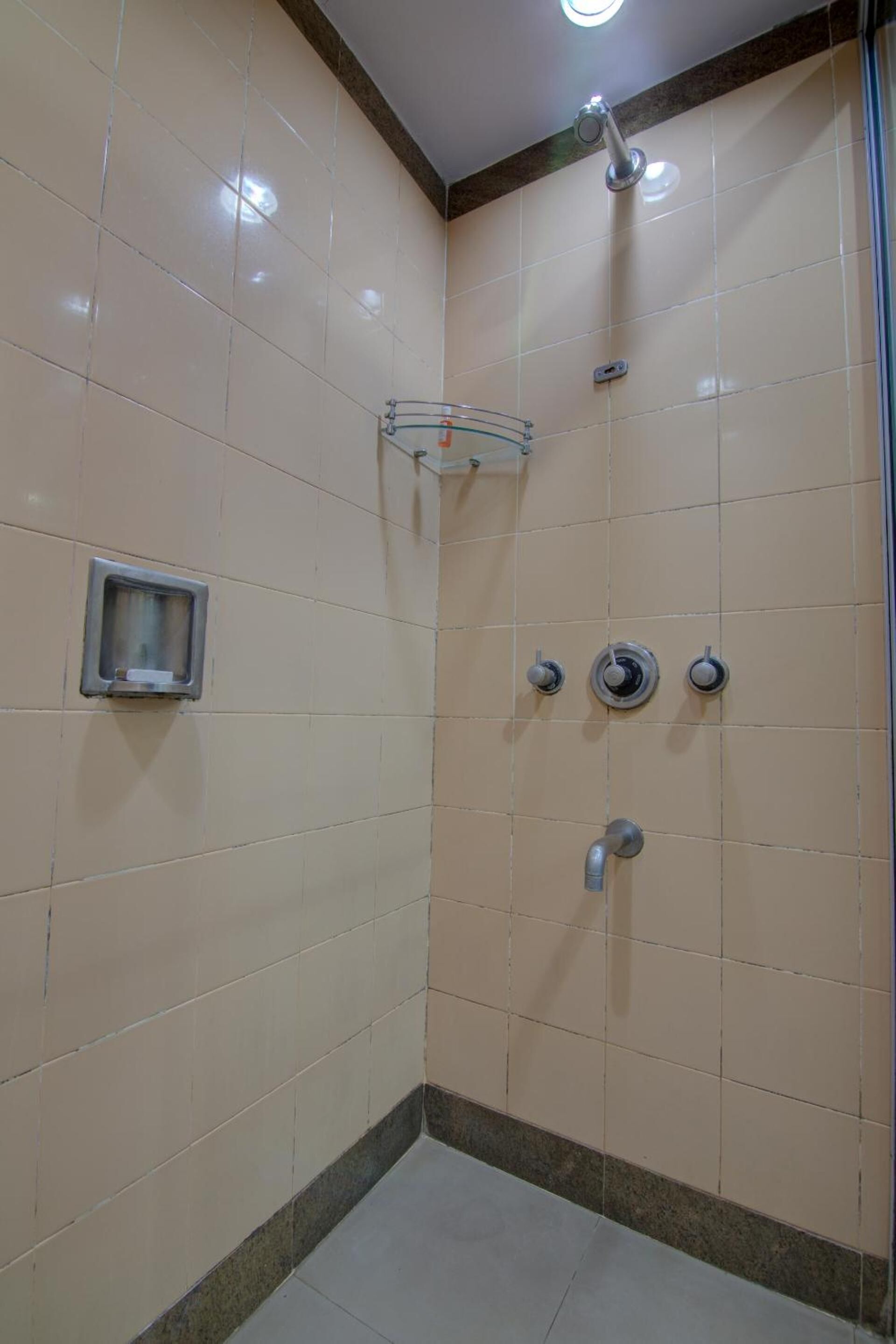 A small, tiled shower area with a glass shelf and a wall-mounted control panel.