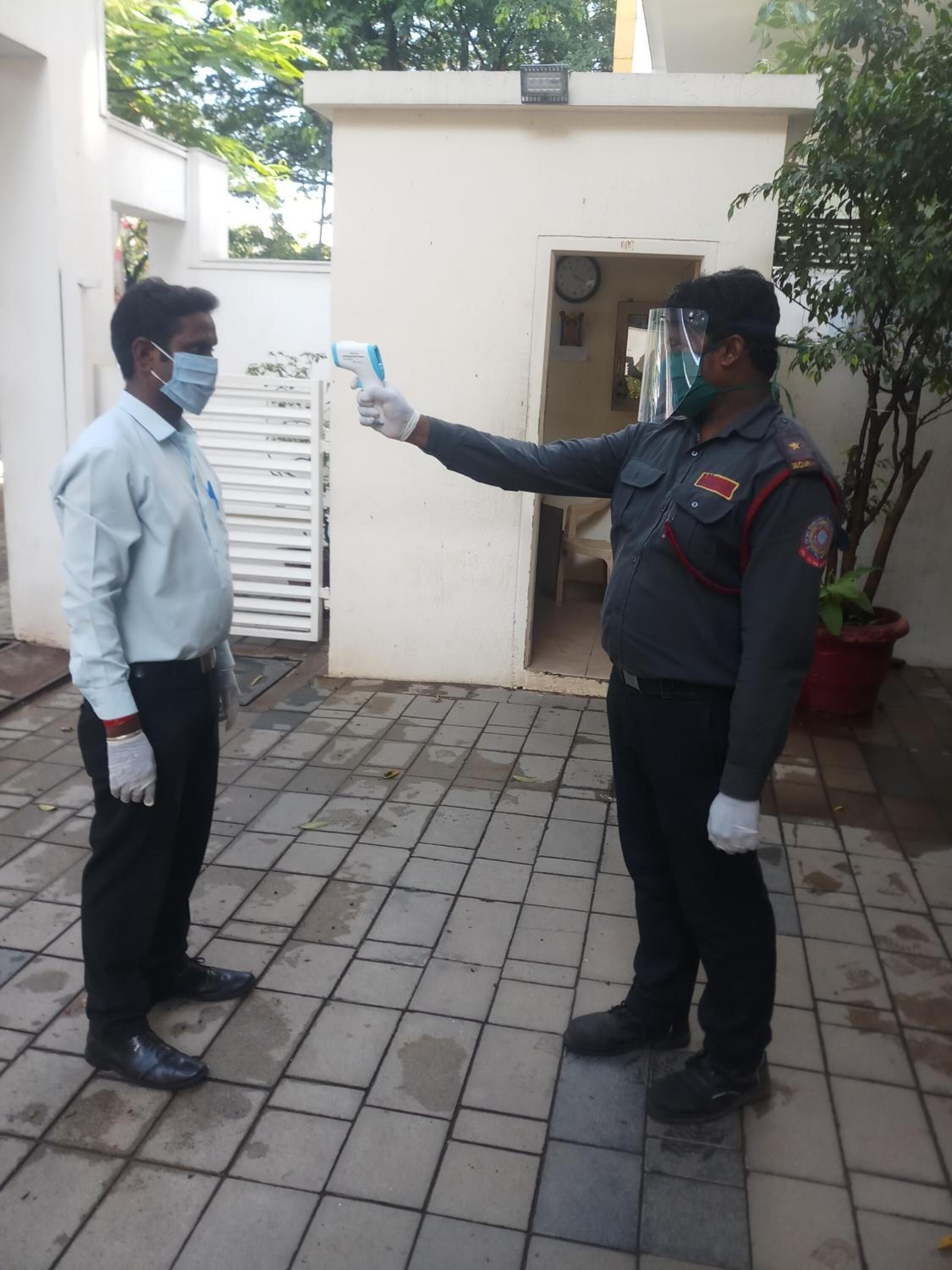 Deux personnes se trouvent dans une cour dont le sol est recouvert de carreaux. L’une d’elles tient un appareil, et on aperçoit une plante en pot à l’arrière-plan.