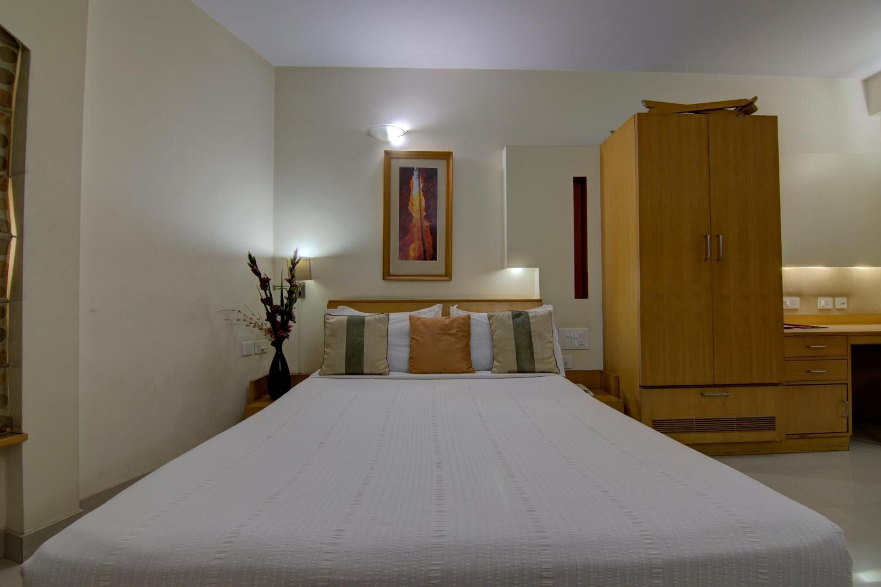 Un dormitorio con una cama grande, un armario de madera, una mesita de noche con una lámpara y un cuadro en la pared.