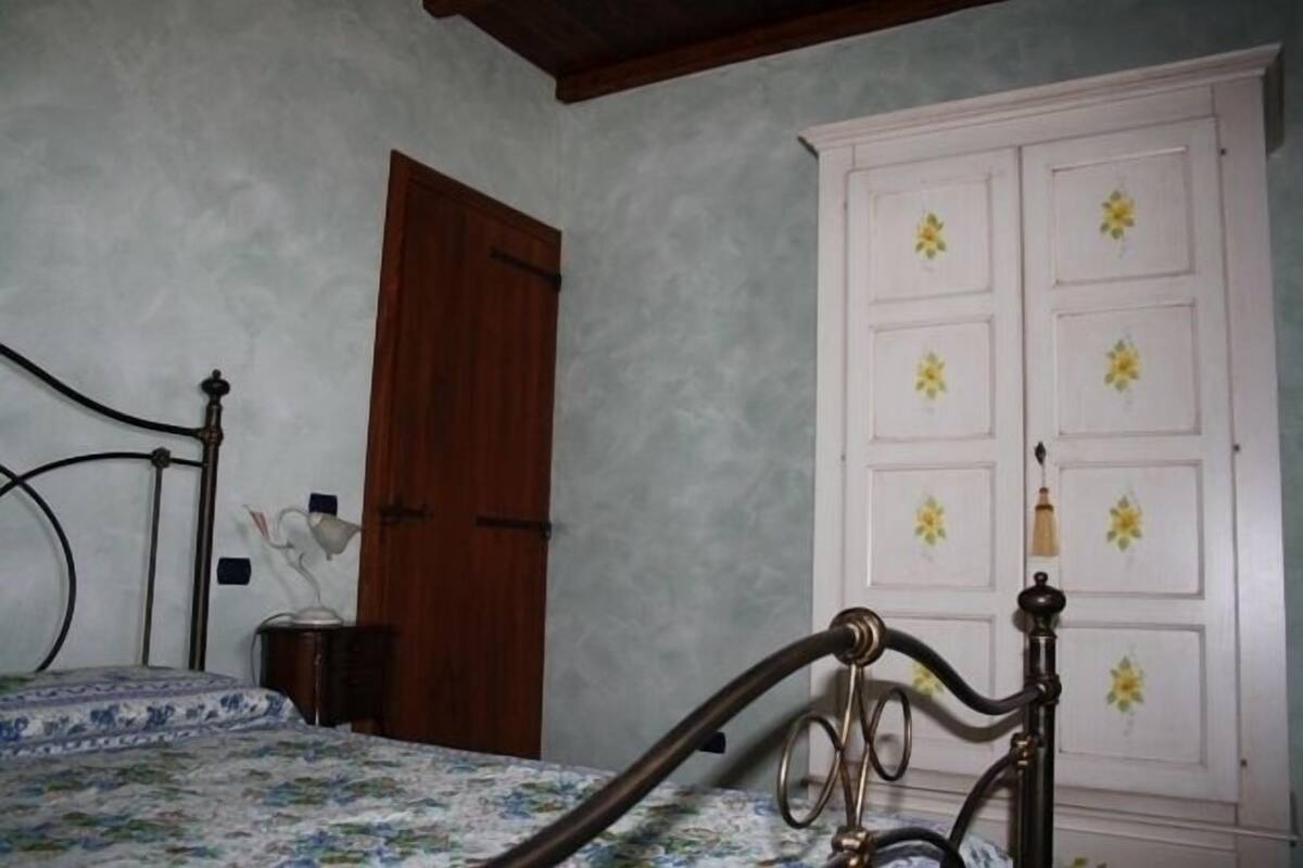 Un dormitorio con cama, puerta de madera, armario blanco con adornos florales y una lámpara de noche.
