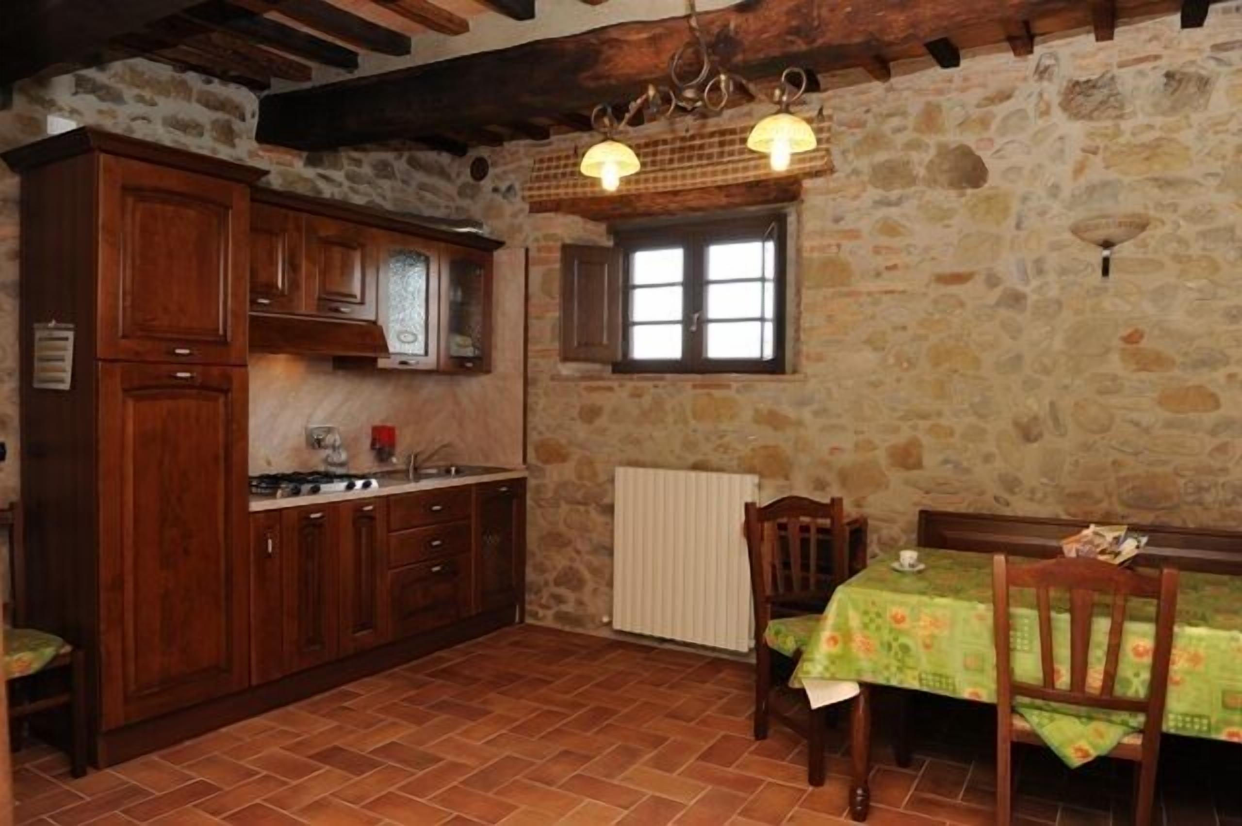 A rustic kitchen with stone walls, wooden cabinets, and a dining area with a table and chairs.