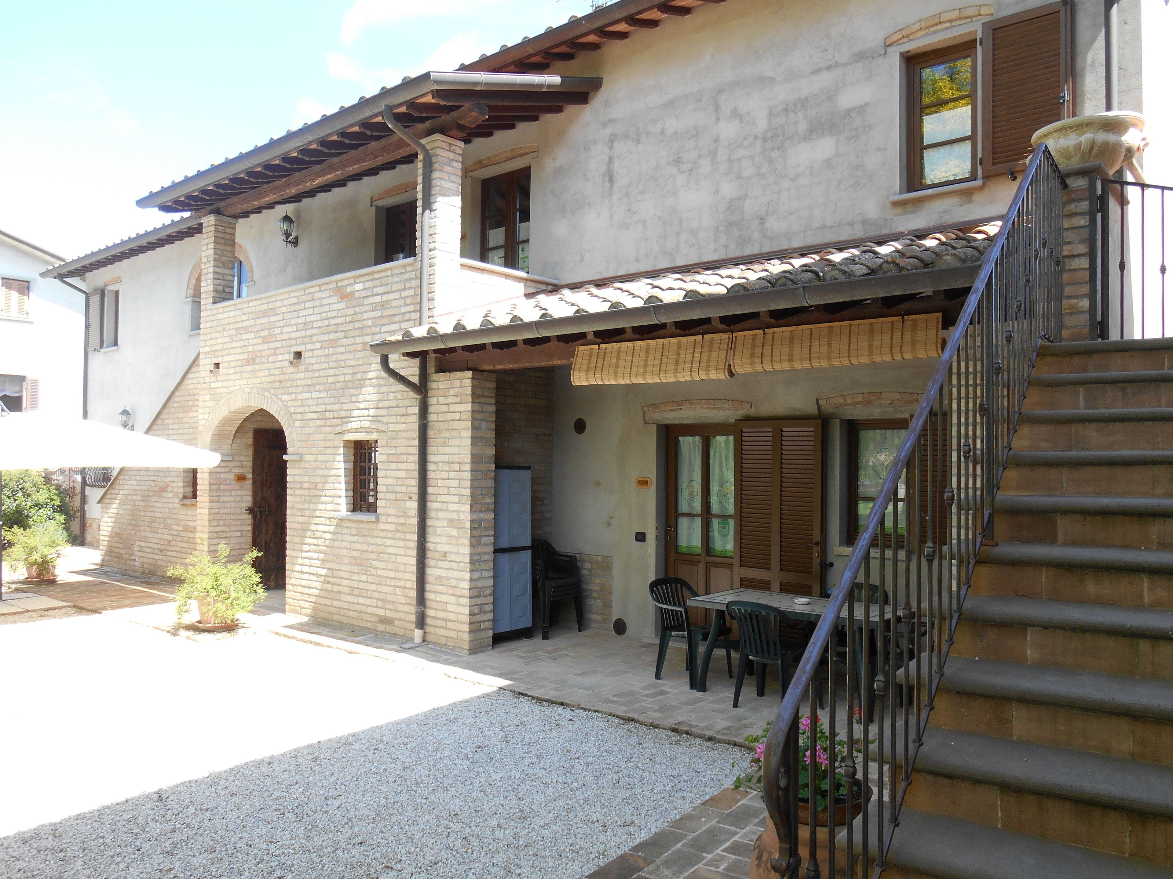 Un bâtiment à deux étages doté d’un patio couvert, d’un espace extérieur aménagé pour s’asseoir et d’un escalier menant à l’étage supérieur.