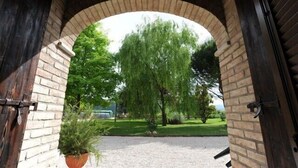 An arched brick entrance with a view of a tree and a grassy area. - Agriturismo Podere Casenove (Citerna)