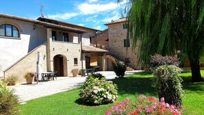 A two-story stone building with a courtyard, outdoor seating, and a large tree. - Agriturismo Podere Casenove (Citerna)