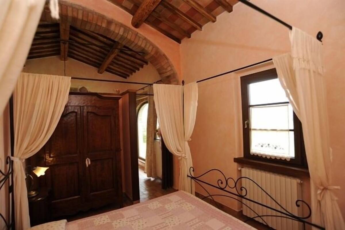 Un dormitorio con un armario de madera, una cama con estructura metálica y una ventana con cortinas.