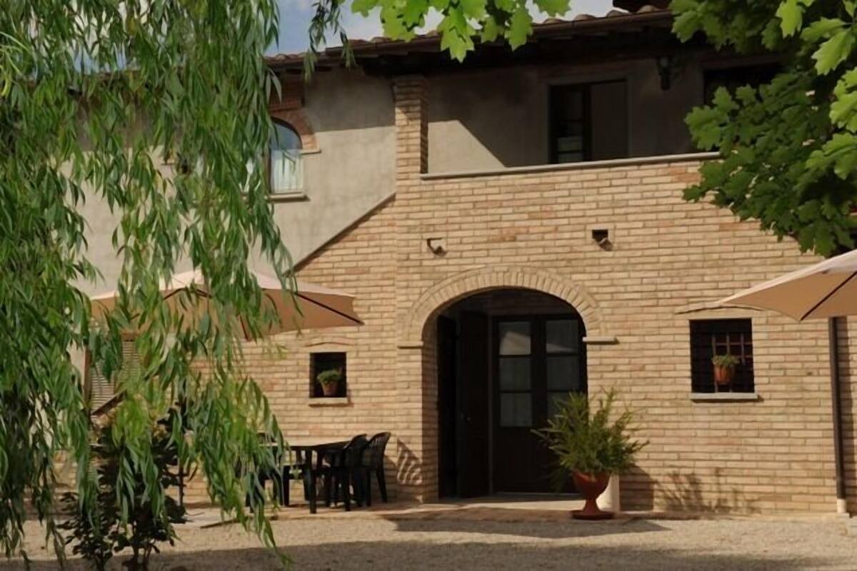 Un edificio de dos pisos con fachada de ladrillo, una puerta negra y un pequeño patio con una mesa y sillas.